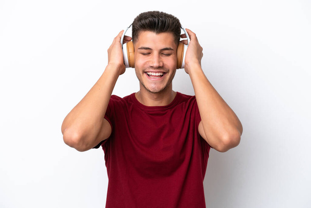Young caucasian man isolated on white background listening music - Fotó, kép