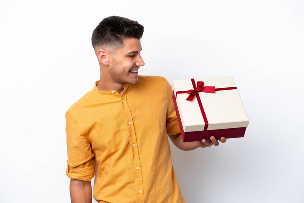 Молодий білий чоловік тримає подарунок ізольований на білому тлі з щасливим виразом
 - Фото, зображення