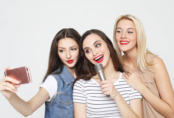 lifestyle, happiness, emotional and people concept: beauty female friends with a microphone singing and take picture with smartphone - Foto, Bild
