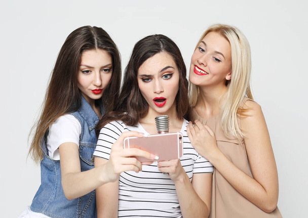 lifestyle, happiness, emotional and people concept: beauty female friends with a microphone singing and take picture with smartphone - Photo, Image