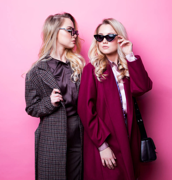 Two sweet young women posing in nice clothes, coat, handbag. Sisters, twins. Spring fashion photo. - Фото, изображение