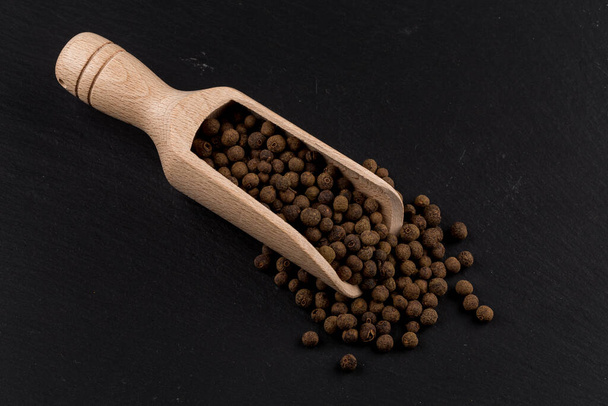 Wooden shovel with large black peppercorn scattered from it - Foto, afbeelding