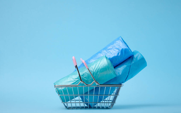 Rolls of plastic bags in a miniature shopping basket on a blue background - Foto, Bild