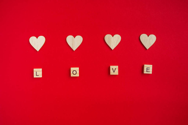 Word LOVE from wooden letters and wooden hearts on a red background. Love, freedom, support, peace symbol. Copy space - Foto, Imagen