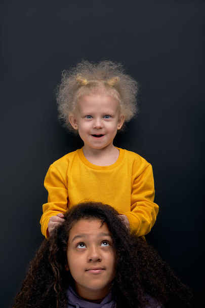 funny little girl with fair fluffy hair doing her sister hair, blonde kid touching her friend hair, head, creation of fashion stylish hairstyle free time, hobby, fun - Foto, Imagem