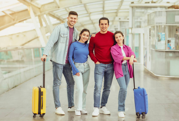 Két utazó pár áll utazási bőröndökkel Mosolyogva a kamerába a modern repülőtéren. Négy fiatalból álló csoport együtt vakációzik. Teljes hosszúságú lövés - Fotó, kép