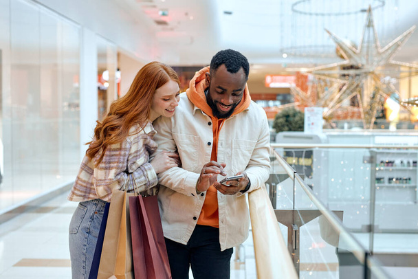 nuoret käyttävät matkapuhelin Holding Värikäs Shopper Laukut seisoo ostoskeskuksessa Onnelliset asiakkaat käyttävät Sovelluksen osto Vaatteet Online Smartphone. Verkkokauppa Shopaholismi. onnellisuus. vapaa-aika - Valokuva, kuva