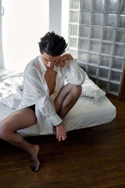 sleepy young gay sits in the bedroom, looks down, full length photo, fashion - Foto, afbeelding