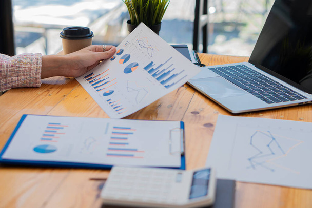Business Finance Manager posiadający dokument wykresu finansowego do analizy miesięcznych wydatków firmy podczas siedzenia w biurze Holding chart i papier graficzny w ręku z laptopem na stole - Zdjęcie, obraz
