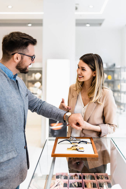 Elegant middle age businessman choosing and buying his new expensive watch. Beautiful young female seller helps him to make good decision. Fashion style and elegance concept. - Valokuva, kuva