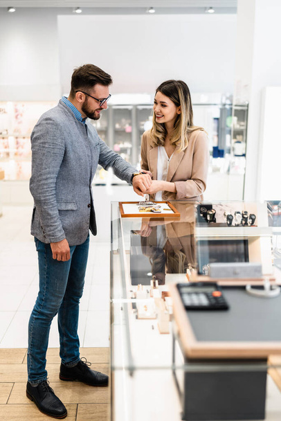 Elegant middle age businessman choosing and buying his new expensive watch. Beautiful young female seller helps him to make good decision. Fashion style and elegance concept. - Foto, imagen