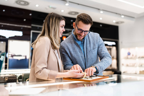 Elegant middle age businessman choosing and buying his new expensive watch. Beautiful young female seller helps him to make good decision. Fashion style and elegance concept. - Foto, imagen