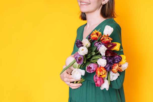 Lady in a green dress with a large bouquet of tulips against a yellow background. - Photo, Image