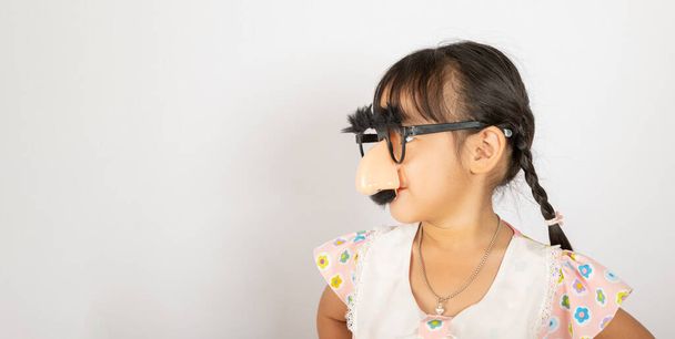 Április elseje. Portré Vicces gyerek lány bohóc visel egy nagy nos és szemüveg, és van egy bajusz elszigetelt fehér háttérrel másolás hely, Boldog mosoly gyermek ünnepi dekoráció - Fotó, kép