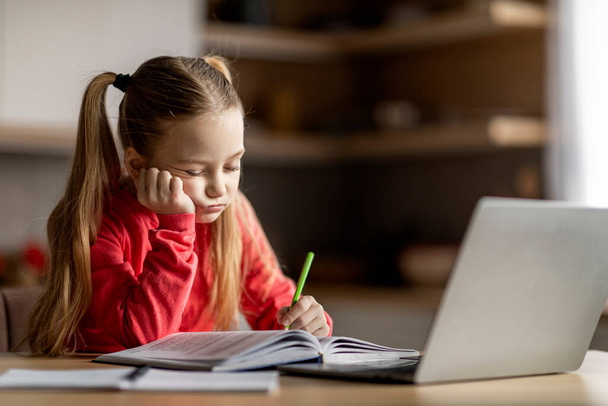 Little cute girl feeling tired and sleepy while doing her homework, exhausted preteen schoolgirl sitting at desk with laptop and falling asleep while writing in book, suffering homeschooling problems - Photo, Image