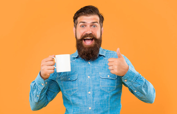 Happy man giving thumbs up holding coffee mug yellow background, copy space. - Foto, immagini