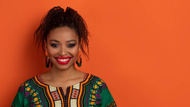 Aito perinteinen kaunis nuori afrikkalainen nainen yllään kirkas asu ja meikki hymyilee kameralle, osoittaa valkoiset terveet hampaat, eristetty oranssi studio tausta, kopioi tilaa, banneri - Valokuva, kuva