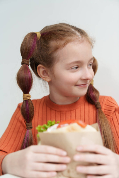 Cute elementary age girl with ponytails eating a sandwich in fast food restaurant. Adorable Ukrainian child eats pita souvlaki dish in Greek cafe - Фото, зображення