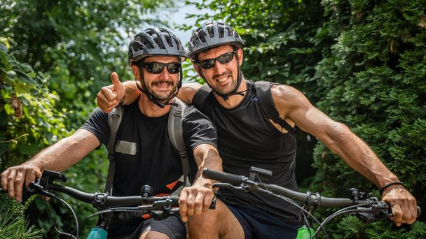 zwei Männer Portrait kaukasischer Freunde männlich vor Elektrorädern E-Bike stehen, während eine Bremse Outdoor-Fahrt in sonnigen Sommertag Schutzhelm tragen - Foto, Bild