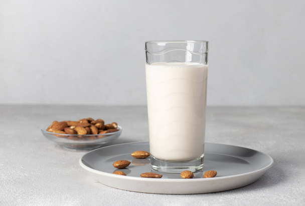 Verse amandelmelk in hoog glas op grijze achtergrond, Gezonde veganistische melkvervanger - Foto, afbeelding