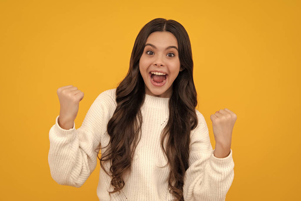 Excited teenager girl. Teenager child overjoyed successful do winner gesture clench fist say yes isolated on yellow background studio - Photo, Image