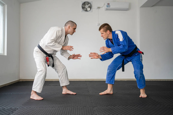 Brazil jiu jitsu bjj edzés vagy kímélve két sportoló harcos kaparja harcművészet technika tornaterem a tatami szőnyeg visel kimono gi fekete öves oktató demonstrálni technika állni - Fotó, kép