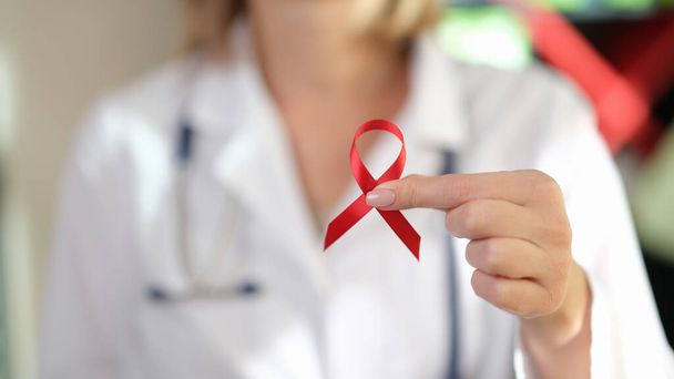Close-up de médico feminino segura fita vermelha em sua mão como símbolo do Dia Internacional da AIDS, consciência do HIV. - Foto, Imagem