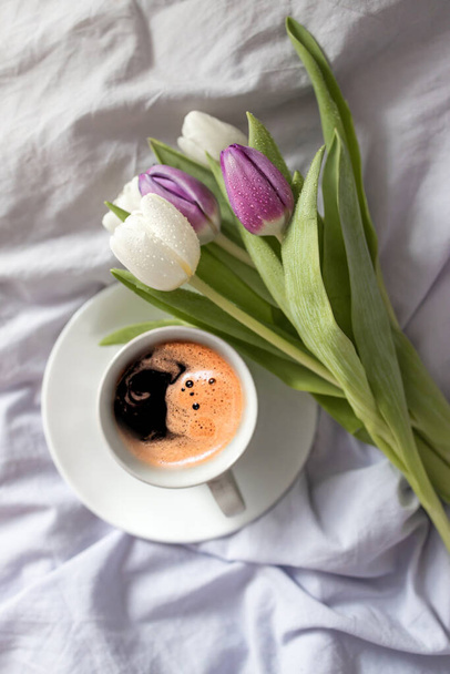 Šálek kávy a čerstvé tulipány na bílém lůžku - Fotografie, Obrázek