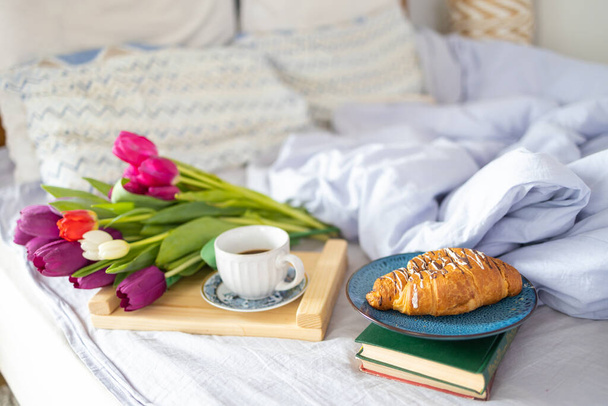 Snídaně podávaná s láskou v posteli, káva, croissant a tulipány na tácu na bílém ložním prádle v romantickém svátečním ránu, kopírovací prostor, vybrané zaměření - Fotografie, Obrázek