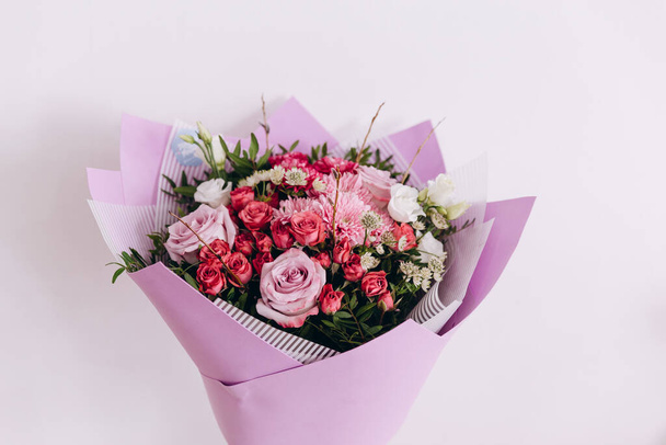 There is a beautiful bouquet of pretty flowers. The bouquet is in a purple-white wrapper on the white background. It is a great present for somebody. It is ready to be bought to the customers. - Foto, Imagem