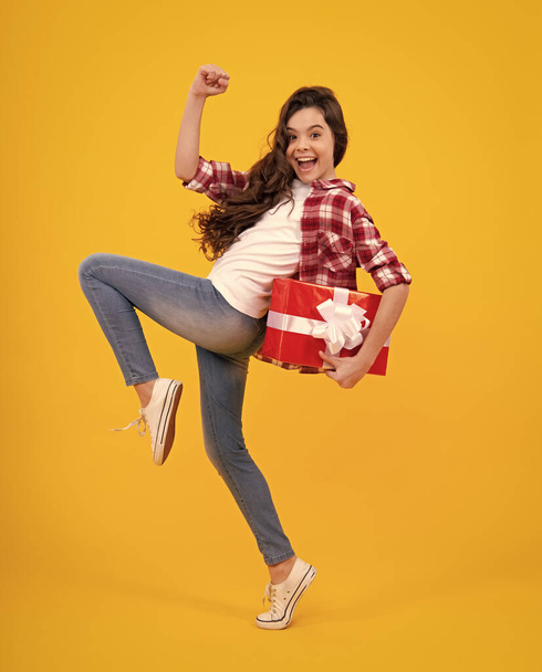 Amazed excited teenage girl child holding gift box on yellow isolated background. Gift for kids birthday. Christmas or New Year present box - Φωτογραφία, εικόνα