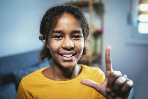Beautiful smiling black deaf girl using sign language at home - Foto, afbeelding