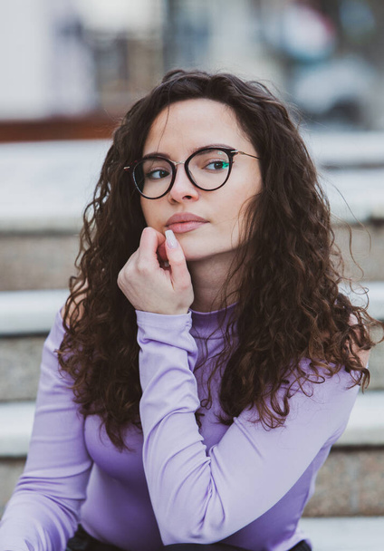 Beautiful young woman with brunette curly hair, portrait in eye glasses enjoying the sun in the city. - Foto, imagen