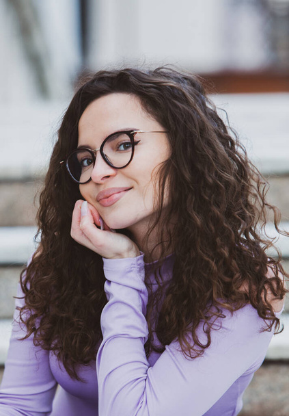 Beautiful young woman with brunette curly hair, portrait in eye glasses enjoying the sun in the city. - Φωτογραφία, εικόνα