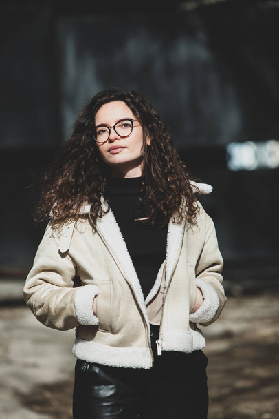 Beautiful young woman with brunette curly hair, portrait in eye glasses enjoying the sun in the city. - Photo, Image
