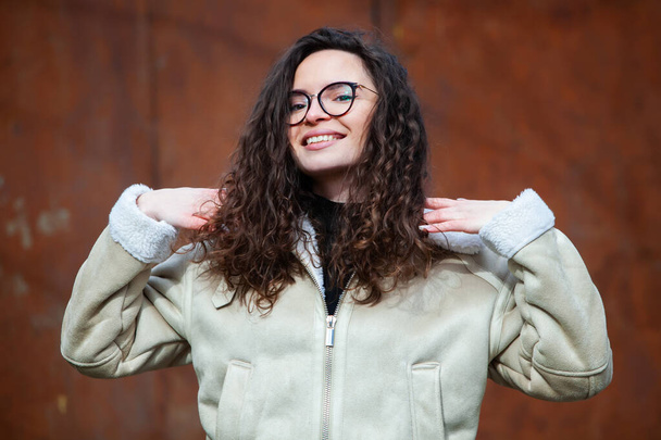 Beautiful young woman with brunette curly hair, portrait in eye glasses enjoying the sun in the city. - Valokuva, kuva