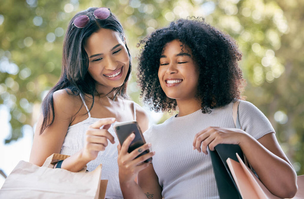 Black woman, shopping and friends with smartphone outdoors for social media retail sales, discount and online fashion deal promo. Planning ecommerce, website shop and browsing internet store together. - Foto, Imagen