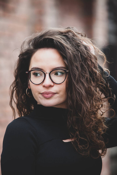 Beautiful young woman with brunette curly hair, portrait in eye glasses enjoying the sun in the city. - Photo, image