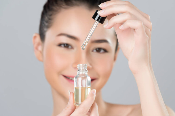 Focus cannabis extracted oil bottle with dropper lid holding by blurred glamorous beautiful asian woman with perfect clean skin and soft smooth makeup in isolated background. - Foto, afbeelding
