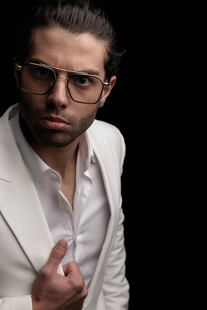 cut out picture of sexy fashion man with glasses holding white jacket suit and posing in front of black background - Photo, image