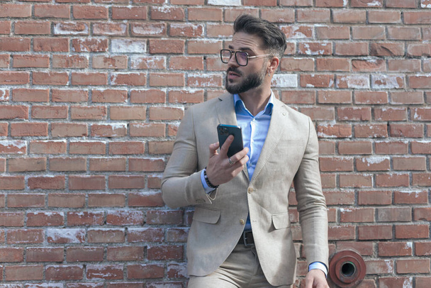 Portrait of handsome businessman texting on phone and being surprised and wearing eyeglasses outdoor, in an old medieval town - Photo, Image
