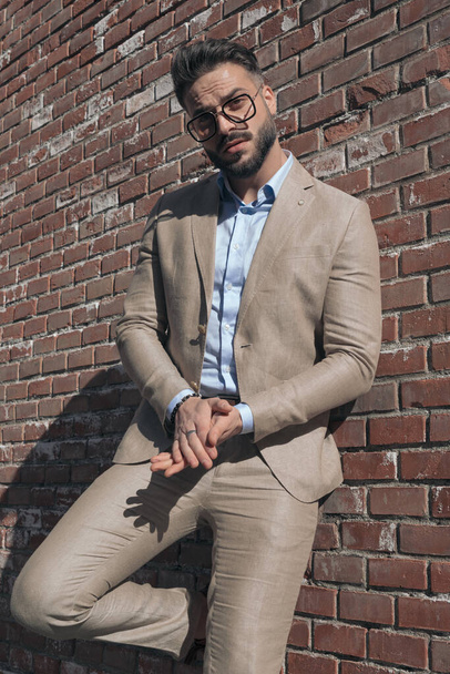 Portrait of handsome businessman rubbing his palms and leaning on brick wall and wearing eyeglasses outdoor, in an old medieval town - Фото, изображение
