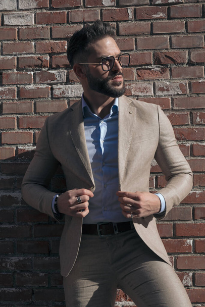 Portrait of sexy businessman arranging his jacket and looking to the side and wearing eyeglasses outdoor, in an old medieval town - Photo, Image