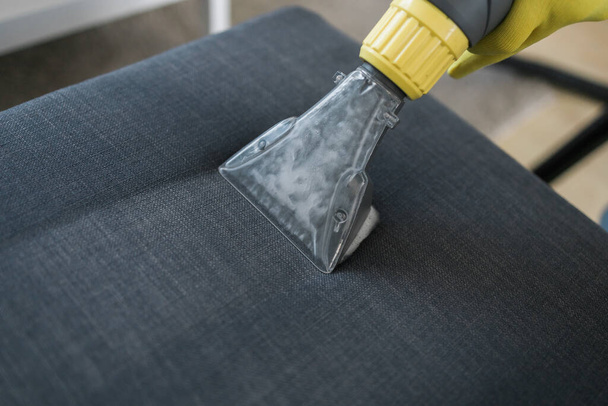 Man in protective rubber glove cleaning sofa with professionally extraction method with washing vacuum cleaner. Early spring regular cleanup. Commercial cleaning company - 写真・画像