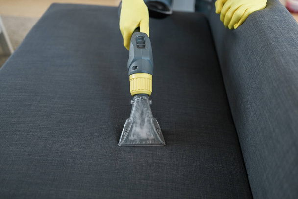 Man in protective rubber glove cleaning sofa with professionally extraction method with washing vacuum cleaner. Early spring regular cleanup. Commercial cleaning company - Foto, imagen