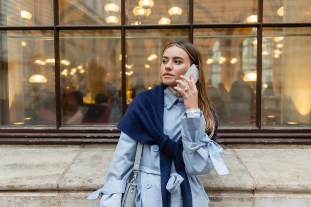 stylish woman with scarf on top of blue trench coat talking on smartphone on street in Vienna - Foto, immagini