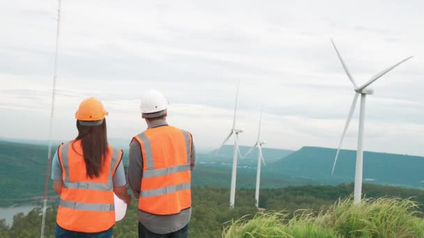 Férfi és női mérnökök dolgoznak egy szélerőműben egy dombon vagy hegyen vidéken. Progresszív ideális a megújuló, fenntartható energia jövőbeli előállításához. - Felvétel, videó