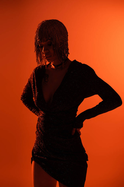 silhouette of woman in black lurex dress and metallic headwear standing with hands on waist on orange background - 写真・画像