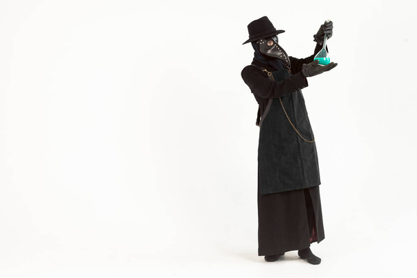 Full-length portrait of a plague doctor from Medieval era holds a glass vessel containing a potion or serum, antidote. Isolated on a white background. epidemic and pandemic concept. - Fotó, kép