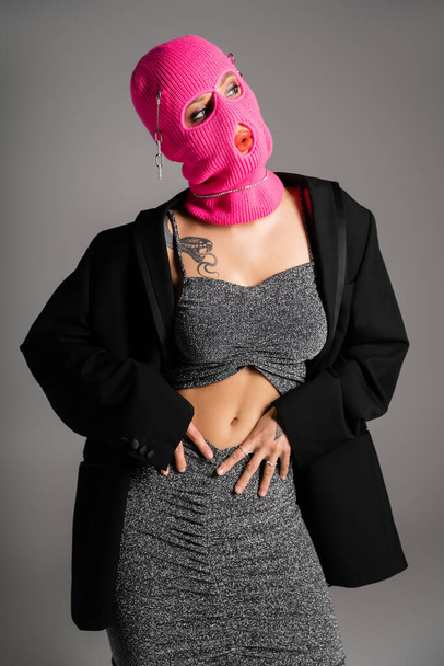 sexy tattooed woman posing in fashionable clothes and pink balaclava isolated on grey - Foto, immagini